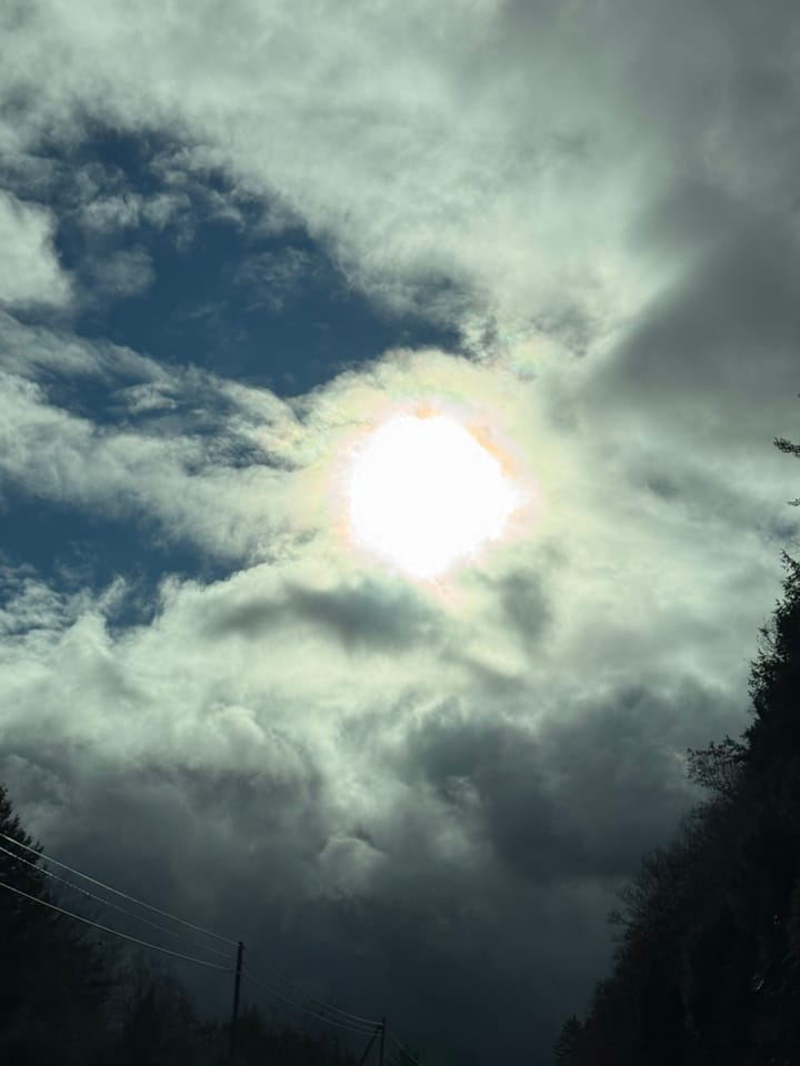 The sun shines through a heavy blanket of dark clouds over a quiet country road—a soft reminder that light from outside always finds its way back in as it meets the light within.