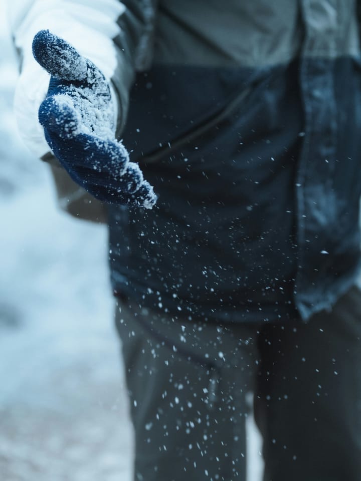 A gloved hand dusted with snow reaching forward, as if offering help on a cold winter day.