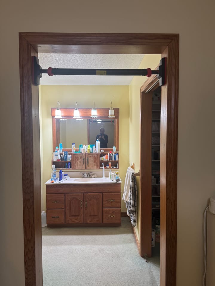 Pull-up bar mounted in a doorway, reflected in a bathroom mirror with the photographer visible in the reflection.