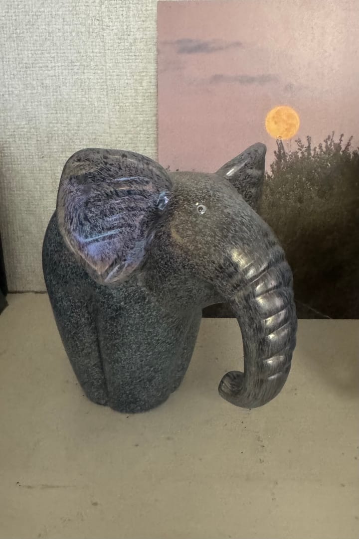 Dark gray glass elephant sculpture with a curved trunk, displayed on a mantel.
